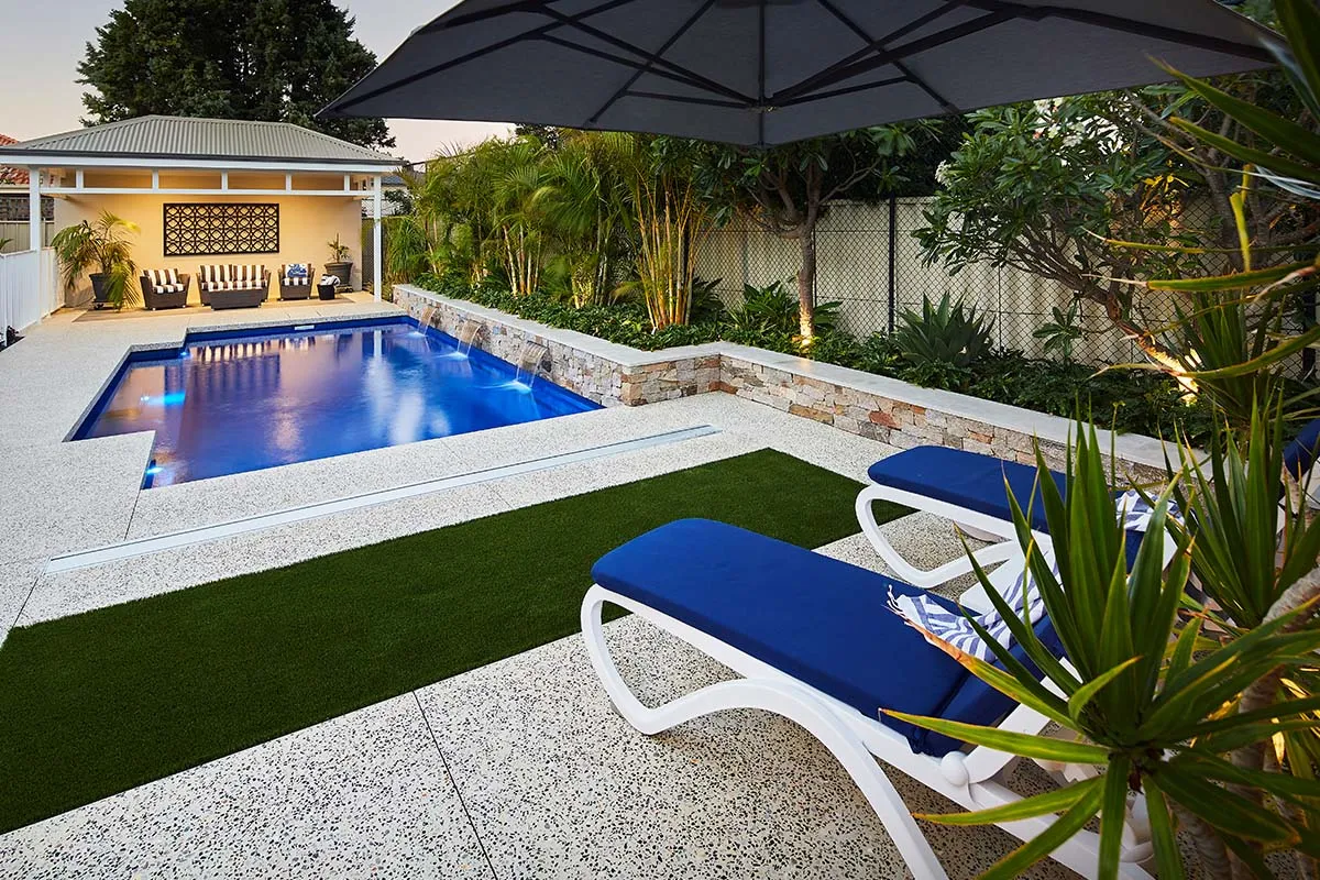 Pool with a lit pavilion, artificial lawn and blue sun loungers on limestone paving