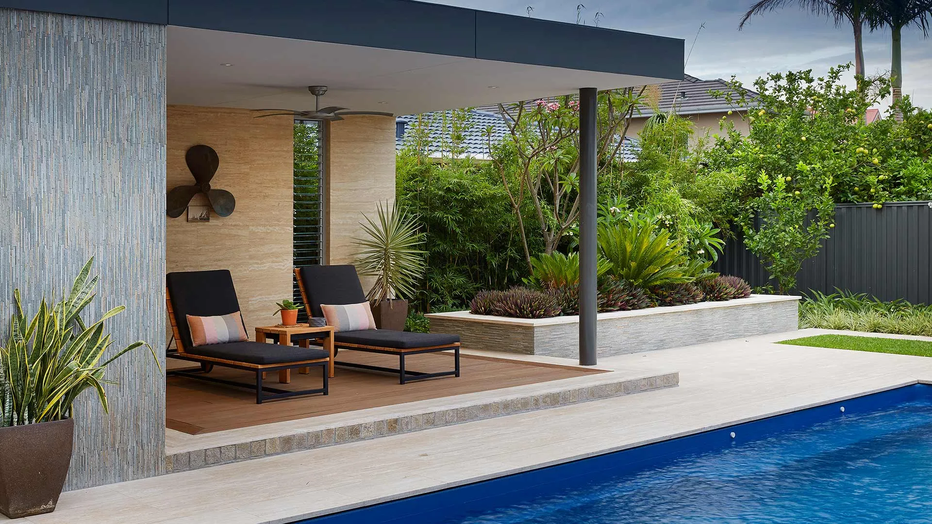 Poolside cabana with sun lounges, travertine paving and lush tropical planting