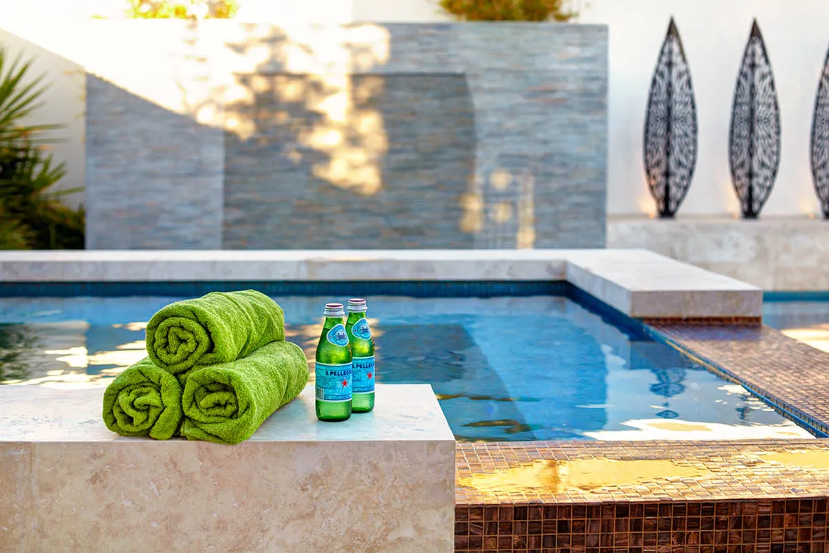 Pool edge with rolled green towels beside a stone clad water feature